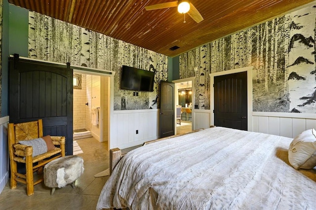 bedroom with a barn door, wainscoting, connected bathroom, wooden ceiling, and wallpapered walls