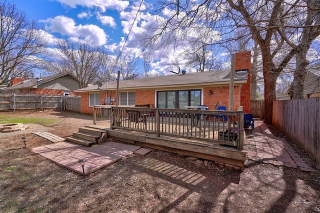 back of house with a fire pit, a fenced backyard, a chimney, a wooden deck, and brick siding