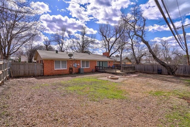 back of house featuring brick siding, a chimney, an outdoor fire pit, a deck, and a fenced backyard