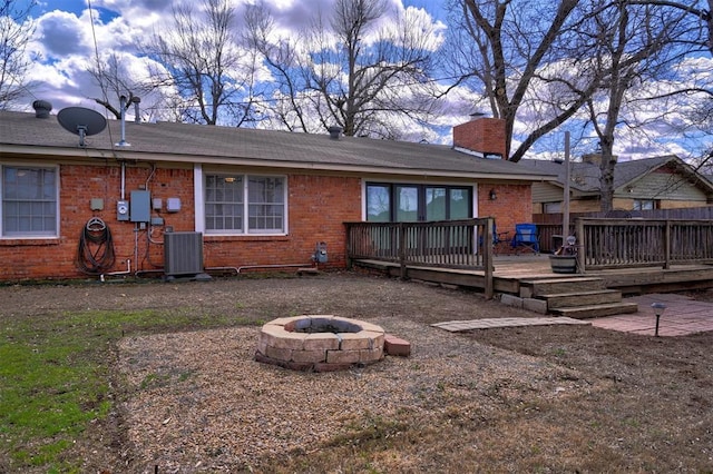 rear view of property featuring brick siding, a chimney, an outdoor fire pit, central AC, and a deck