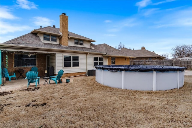 back of house featuring a shingled roof, a fenced in pool, fence, and a chimney