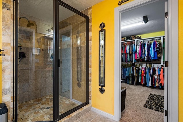 bathroom featuring a walk in closet, a shower stall, baseboards, and a textured ceiling