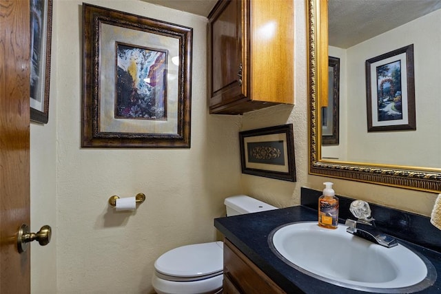 half bathroom with a textured ceiling, toilet, vanity, and a textured wall