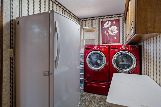 washroom with washing machine and clothes dryer, cabinet space, and wallpapered walls