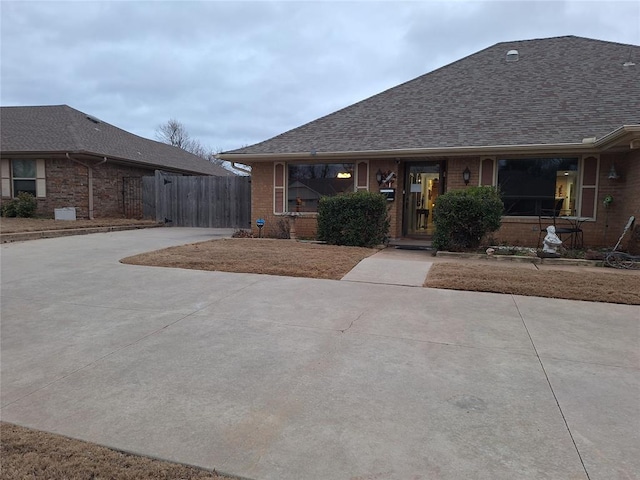 ranch-style home with fence, brick siding, driveway, and a shingled roof