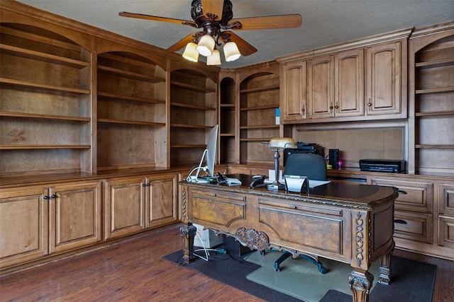 home office with a ceiling fan, built in desk, dark wood-style flooring, and a textured ceiling