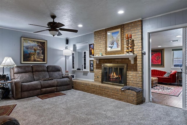 carpeted living room with visible vents, ceiling fan, ornamental molding, a fireplace, and a textured ceiling