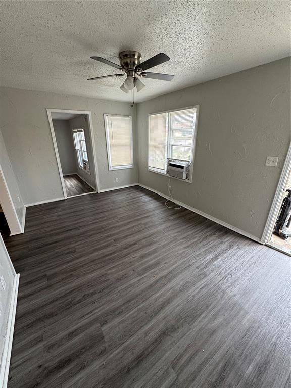 empty room featuring a textured ceiling, dark wood finished floors, and a healthy amount of sunlight