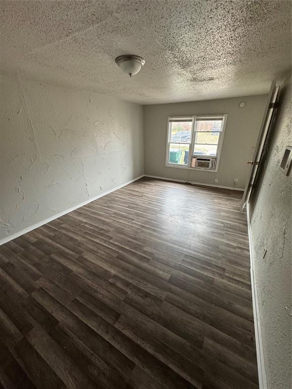 spare room featuring dark wood-style floors, a textured wall, a textured ceiling, and baseboards