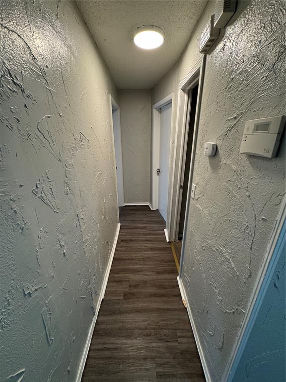 hallway with a textured ceiling, a textured wall, dark wood finished floors, and baseboards