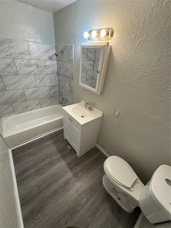 bathroom with tub / shower combination, a textured wall, toilet, and wood finished floors