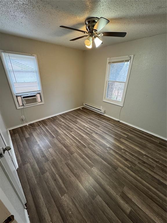 spare room with a baseboard heating unit, dark wood-type flooring, a textured ceiling, and cooling unit