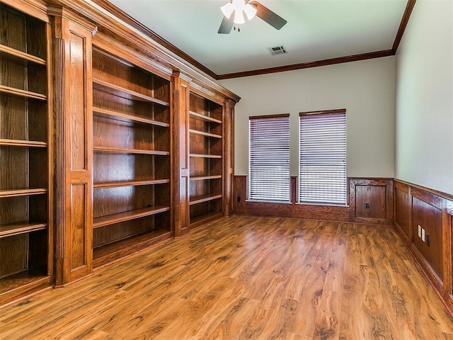 unfurnished living room with a wainscoted wall, visible vents, ornamental molding, ceiling fan, and wood finished floors