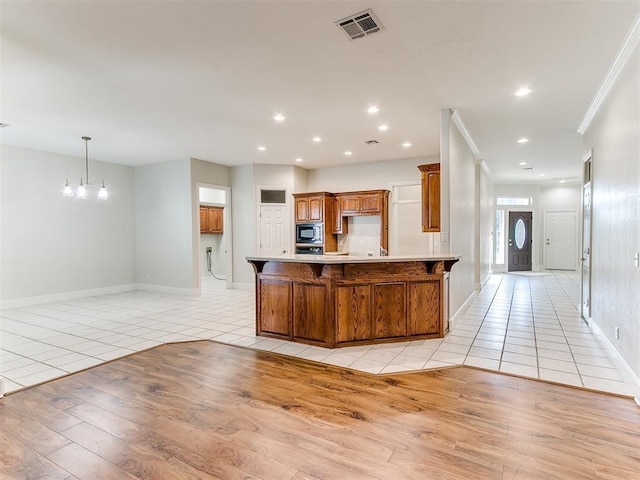 kitchen featuring light tile patterned floors, visible vents, light countertops, built in microwave, and brown cabinetry