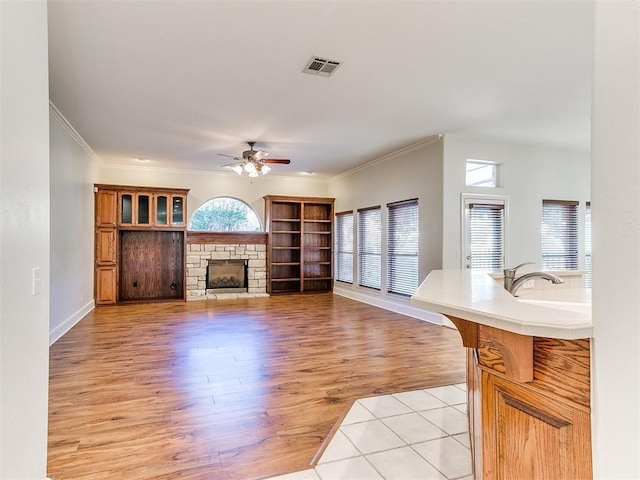 living area with ceiling fan, light wood-style flooring, a fireplace, visible vents, and crown molding