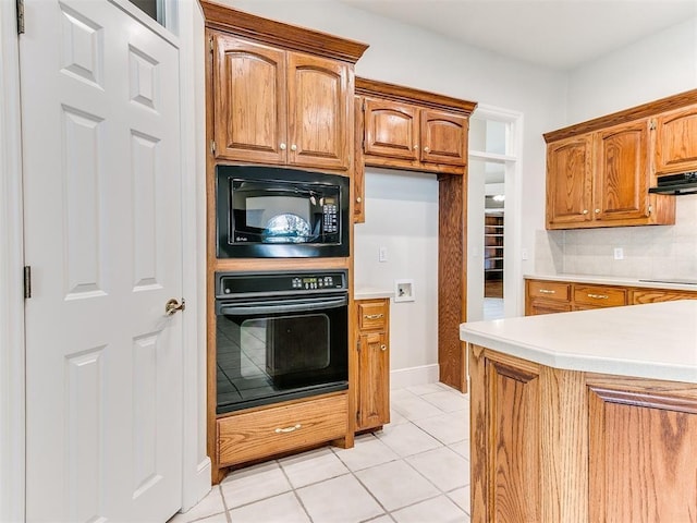 kitchen featuring tasteful backsplash, light countertops, light tile patterned flooring, under cabinet range hood, and black appliances