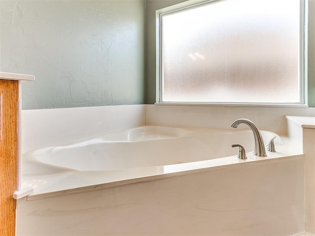 bathroom with a wealth of natural light, a textured wall, and a bath