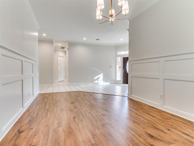 empty room featuring a chandelier, a decorative wall, light wood finished floors, and ornamental molding