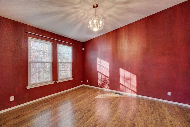 unfurnished room featuring baseboards, visible vents, an inviting chandelier, and wood finished floors