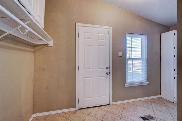 entrance foyer with light tile patterned floors, baseboards, visible vents, and vaulted ceiling