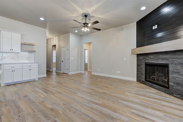 unfurnished living room featuring baseboards, light wood-type flooring, a stone fireplace, recessed lighting, and a ceiling fan