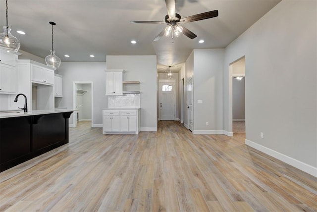 kitchen with open shelves, light countertops, white cabinetry, light wood-type flooring, and backsplash