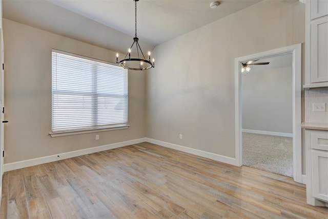 unfurnished dining area with ceiling fan with notable chandelier, light wood-type flooring, and baseboards