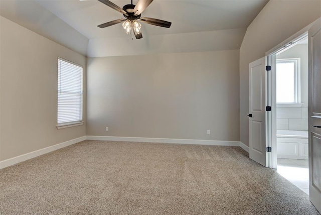 spare room featuring plenty of natural light, light colored carpet, lofted ceiling, and baseboards