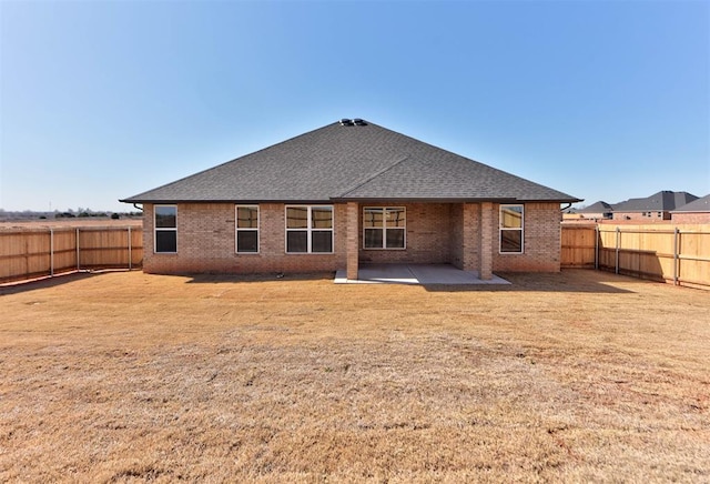 back of property with a patio, brick siding, roof with shingles, and a fenced backyard