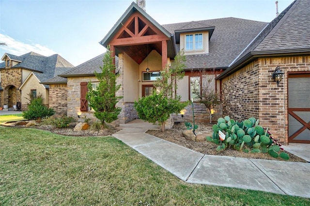 view of front of property featuring a shingled roof, stone siding, stucco siding, a front yard, and brick siding