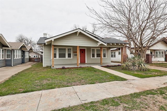 bungalow-style home featuring covered porch, a front lawn, and a chimney