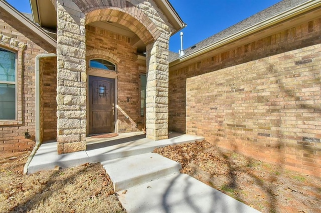 view of exterior entry with roof with shingles and brick siding