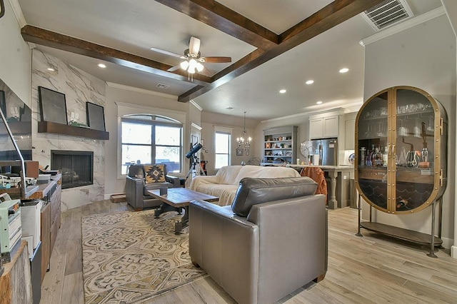 living area featuring beam ceiling, visible vents, light wood-style flooring, a high end fireplace, and ceiling fan with notable chandelier