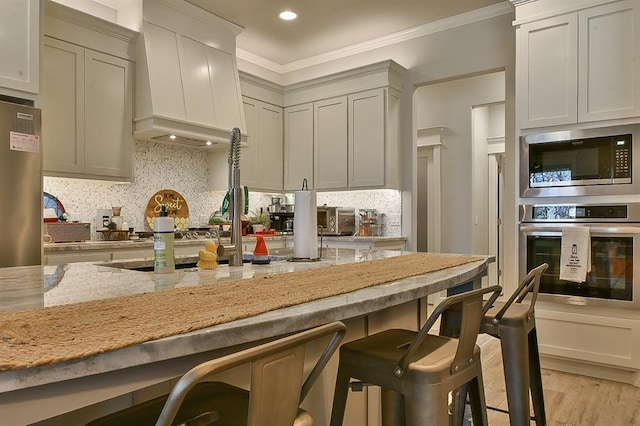 kitchen featuring stainless steel appliances, a kitchen breakfast bar, custom exhaust hood, light stone countertops, and tasteful backsplash