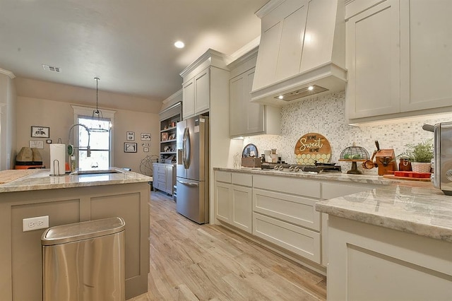 kitchen with light wood finished floors, visible vents, appliances with stainless steel finishes, premium range hood, and a sink