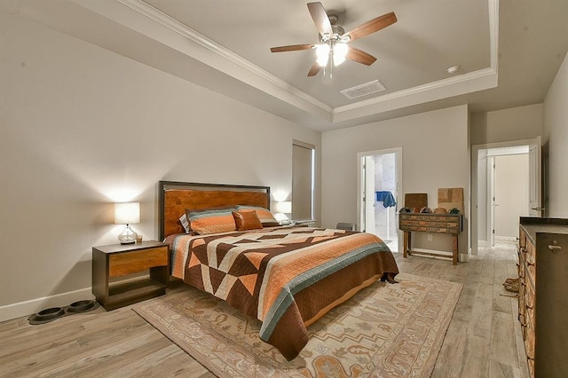 bedroom with visible vents, baseboards, light wood-style floors, a tray ceiling, and crown molding