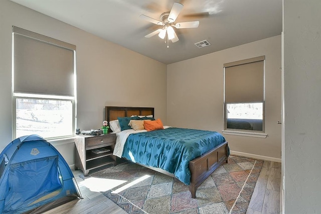 bedroom with ceiling fan, wood finished floors, visible vents, and baseboards