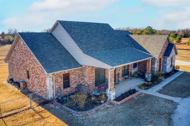 view of front of home featuring a patio, roof with shingles, fence, a front yard, and brick siding