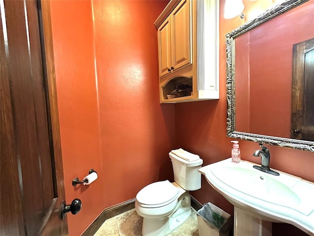 half bath with toilet, baseboards, and a sink