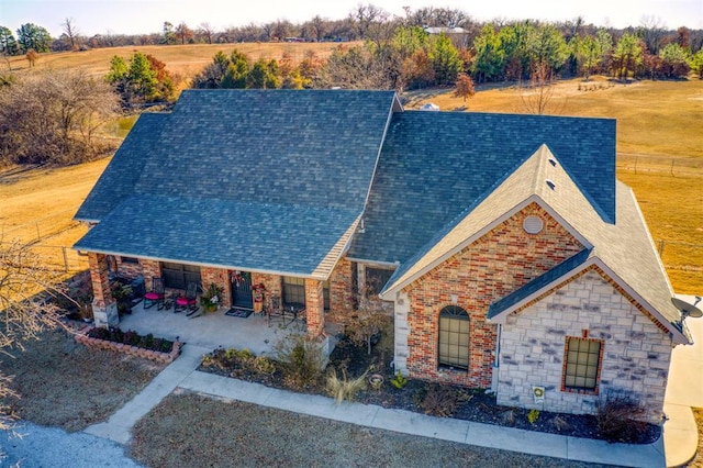 exterior space featuring a patio, brick siding, stone siding, roof with shingles, and a front yard