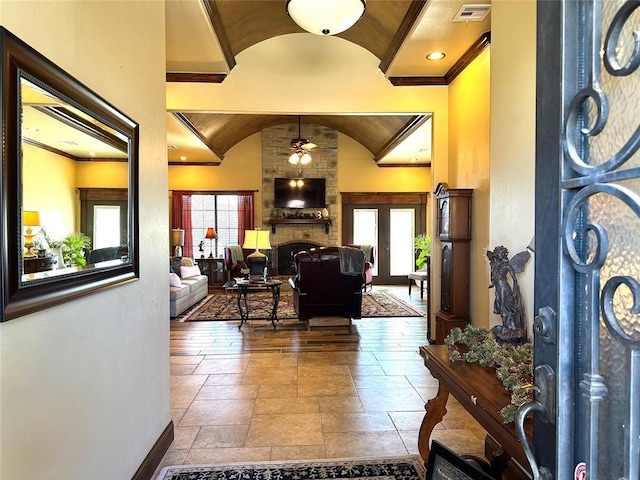 foyer entrance with stone tile floors, a large fireplace, a ceiling fan, baseboards, and vaulted ceiling