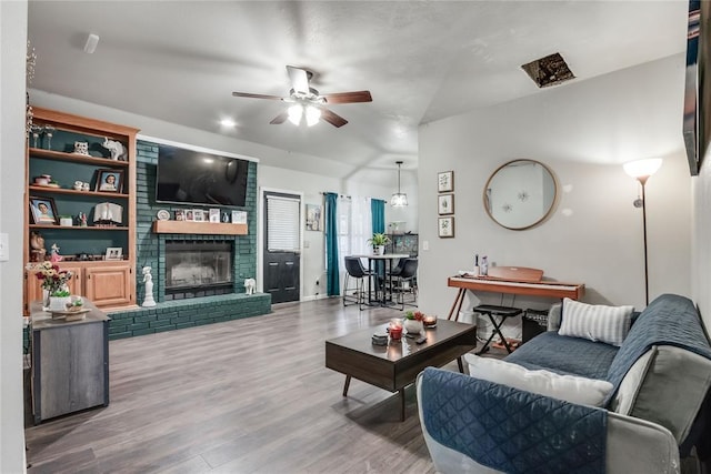 living area featuring ceiling fan, lofted ceiling, a fireplace, and wood finished floors