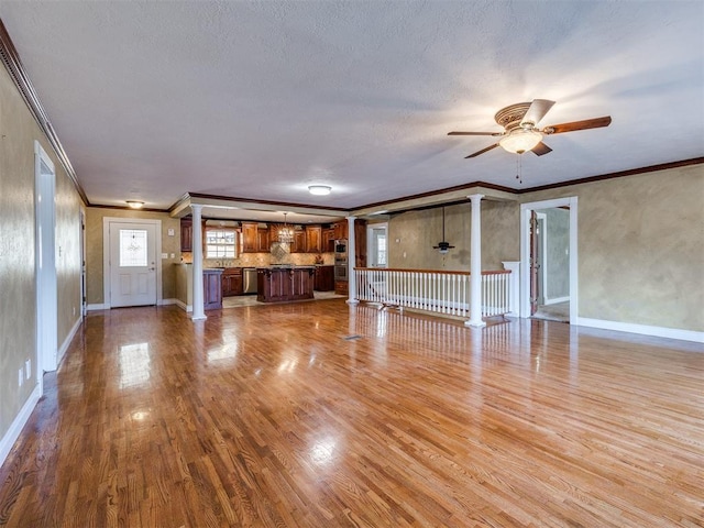 unfurnished living room featuring decorative columns, baseboards, ceiling fan, ornamental molding, and wood finished floors