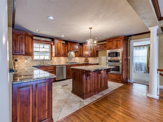 kitchen featuring stainless steel appliances, a sink, light wood finished floors, decorative columns, and tasteful backsplash