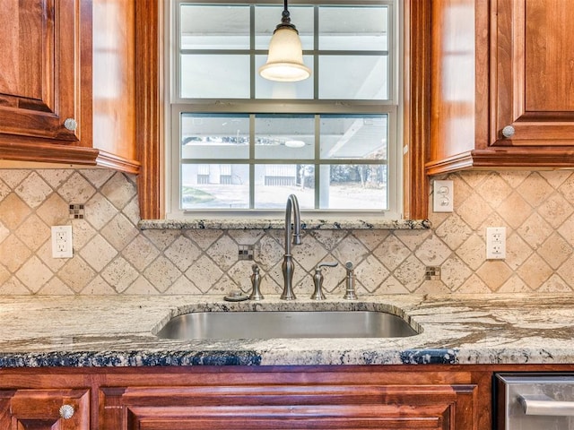 kitchen with tasteful backsplash, brown cabinetry, light stone counters, decorative light fixtures, and a sink