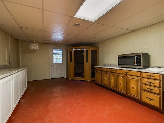 interior space with concrete flooring, brown cabinets, stainless steel microwave, and a drop ceiling