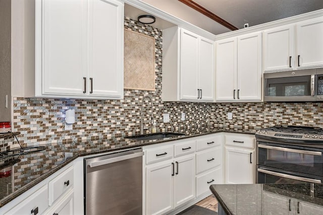 kitchen with tasteful backsplash, appliances with stainless steel finishes, white cabinetry, a sink, and dark stone countertops