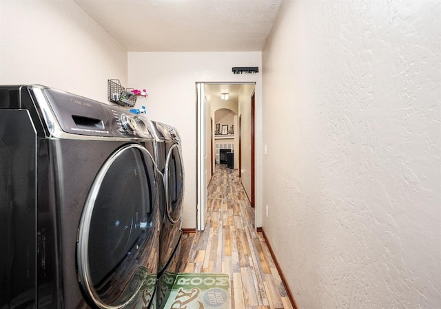 clothes washing area with a textured wall, laundry area, wood finished floors, baseboards, and independent washer and dryer