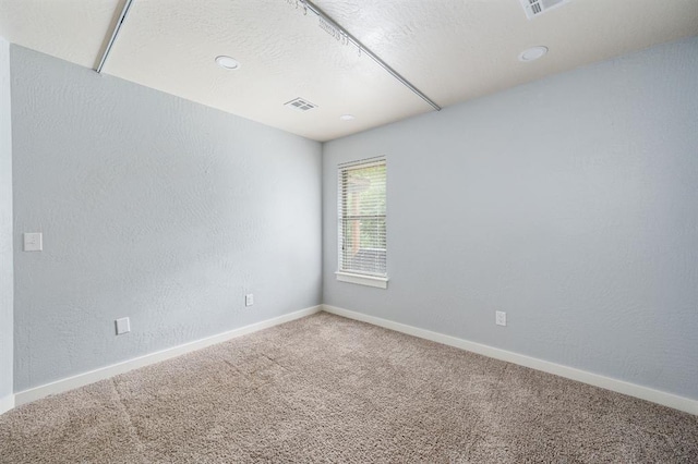 empty room featuring carpet, visible vents, a textured wall, and baseboards