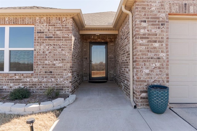 view of exterior entry with a shingled roof, brick siding, and an attached garage